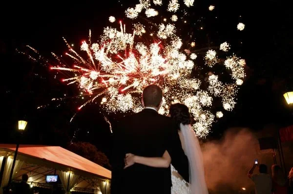 Novios saliendo mientras un show pirotécnico ilumina el cielo